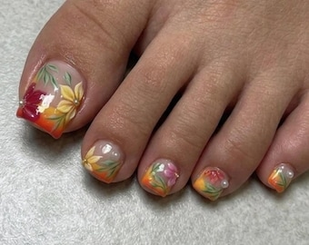 Puede incluir: Primer plano de un pie con uñas pintadas. Las uñas presentan un diseño floral con degradados amarillos, rojos y naranjas. Algunas uñas tienen pequeños detalles de perlas. El diseño incluye hojas y flores.