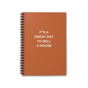 May include: A spiral-bound notebook with a burnt orange cover. The cover features the text "IT'S A GREAT DAY TO SELL A HOUSE" in white. The notebook's spiral binding is black.