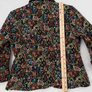 May include: A floral tapestry jacket with a black background and a colorful pattern of roses and other flowers in shades of red, green, purple, and yellow. The jacket has long sleeves and a collar. The ruler shows the jacket is approximately 20 inches long.