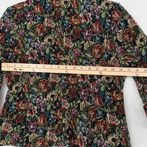 May include: A floral tapestry jacket with a colorful pattern of red, green, and purple flowers. The jacket has long sleeves and a tailored fit. A wooden ruler is placed across the jacket, measuring approximately 19 inches.