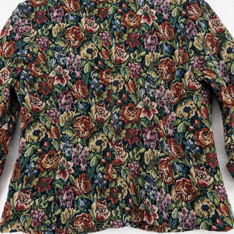 May include: A tapestry jacket with a floral pattern. The jacket features a dark background with a dense arrangement of flowers in shades of red, orange, yellow, purple, and blue. The sleeves are long and the jacket is tailored.