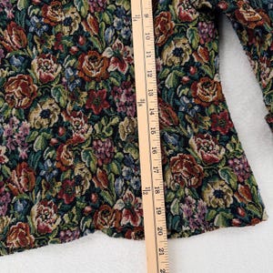 May include: A floral tapestry jacket with a colorful pattern of roses and other flowers in shades of red, green, and brown. The jacket is measured with a wooden ruler, showing a length of approximately 21 inches.