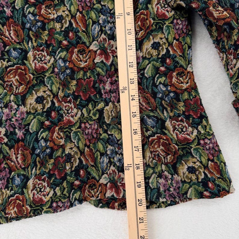 May include: A floral tapestry jacket with a colorful pattern of roses and other flowers in shades of red, green, and brown. The jacket is measured with a wooden ruler, showing a length of approximately 21 inches.