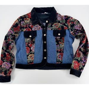 May include: A cropped denim jacket with floral velvet sleeves and accents. The jacket features a black velvet collar, trim, and pockets. The floral pattern includes red, pink, and purple roses on a black background. Silver buttons run down the front.
