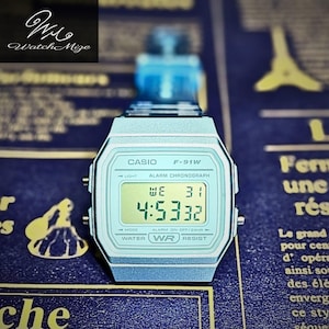 May include: A light blue Casio F-91W digital watch showing the time 4:53:32. The watch has a rectangular face with a digital display and a silver-tone strap. The watch face includes the Casio logo and the text "WATER WR RESIST".