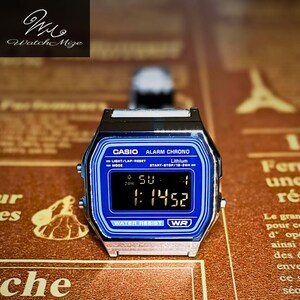 以下が含まれることがあります： 青い文字盤とシルバーカラーのケースを備えたデジタルCasio Alarm Chrono腕時計。 時計は1:14:52の時刻を表示します。 時計の文字盤には「CASIO ALARM CHRONO」と「WATER RESIST WR」の文字があります。 ブランド名「Watch Mize」は左上にあります。