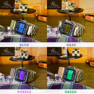 May include: A silver digital watch with a rectangular face and a metal strap. The watch face shows a blue digital time. The image also shows silver cufflinks and a small black display stand. The watch is a classic design.