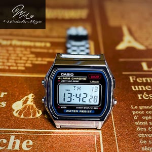 May include: A silver Casio digital watch with a black and blue face showing the time 13:42:28. The watch has a rectangular case and a stainless steel strap. The watch face includes the text "CASIO", "ALARM CHRONO", and "WATER RESIST".