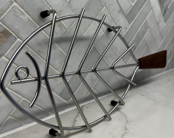 Salvamanteles vintage de alambre metálico con forma de pez y mango de madera de teca, fabricado en Dinamarca, estilo escandinavo.
