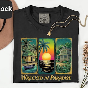 May include: Black t-shirt with a colorful graphic of a tropical scene, including a sunset, palm trees, and a house. The text "Wrecked in Paradise" is printed below the graphic. A gold necklace with a star pendant is on the shirt.
