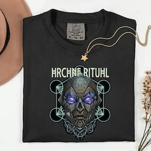 May include: Black t-shirt with a geometric skull design and the text "HRCHNE RITUAL". A gold star pendant necklace rests on the shirt. The shirt is a Comfort Colors XL.