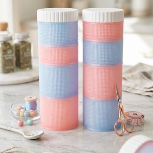 May include: Two pastel-colored storage containers stacked with pink, blue, and lavender sections. Each container has a white lid. The containers are on a white surface with a tag that reads "Organized / Beautifully Stored."