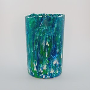 Könnte beinhalten: Ein zylindrischer Becher mit einem marmorierten Design in Blau-, Grün- und Weißtönen. Die Farben sind ineinander gewirbelt und erzeugen ein einzigartiges Muster. Der obere Rand des Bechers hat eine leicht unebene Textur.