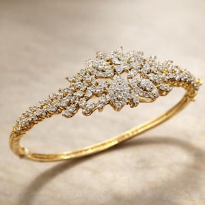 May include: A gold-toned bracelet with a floral design. The bracelet features a series of small, sparkling stones clustered together to form a decorative pattern. The band is smooth and polished, creating a contrast with the textured design.