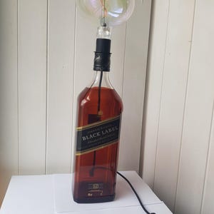May include: A repurposed lamp made from a Johnnie Walker Black Label whiskey bottle. The lamp features a large, round, clear light bulb and a black cord with an on/off switch. The bottle is filled with a dark liquid.
