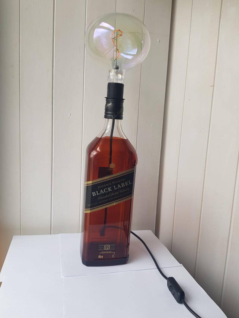May include: A repurposed lamp made from a Johnnie Walker Black Label whiskey bottle. The lamp features a large, round, clear light bulb and a black cord with an on/off switch. The bottle is filled with a dark liquid.