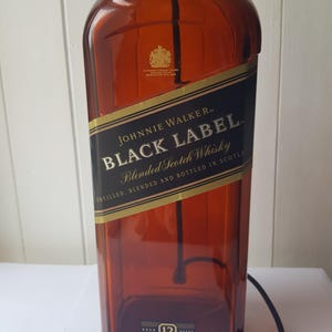 May include: A large, amber-colored Johnnie Walker Black Label whisky bottle. The label features gold and black text, including "Black Label" and "Blended Scotch Whisky." The bottle is marked "12" and "3L."