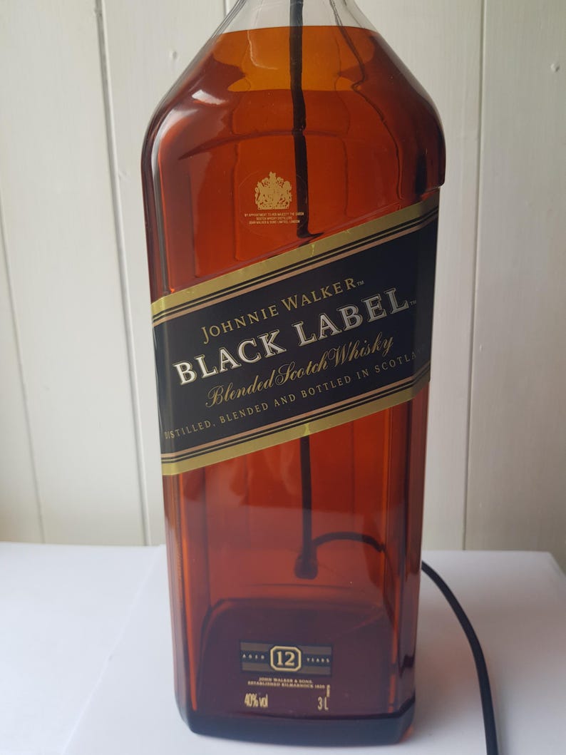 May include: A large, amber-colored Johnnie Walker Black Label whisky bottle. The label features gold and black text, including "Black Label" and "Blended Scotch Whisky." The bottle is marked "12" and "3L."