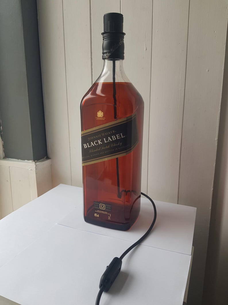 May include: A repurposed Johnnie Walker Black Label whiskey bottle transformed into a lamp. The amber-colored glass bottle features a black label with gold lettering. A black lamp socket and cord with an on/off switch are attached.
