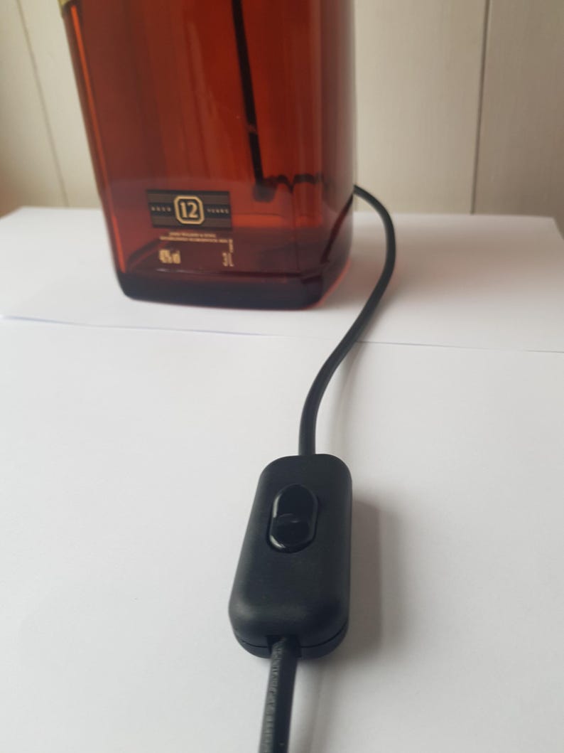 May include: A brown glass bottle with a black power cord and switch. The bottle has a label with the number 12 and other text. The switch is black and oval-shaped.