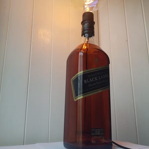 May include: A repurposed lamp made from a Johnnie Walker Black Label whiskey bottle. The brown glass bottle has a black label and a large, round lightbulb. The lamp is plugged in and ready to use.