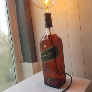 May include: A unique lamp made from a Johnnie Walker Black Label bottle. The brown glass bottle is topped with a large, round lightbulb with a decorative filament. A black cord with an on/off switch extends from the bottle.