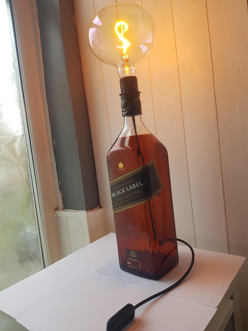 May include: A unique lamp made from a Johnnie Walker Black Label bottle. The brown glass bottle is topped with a large, round lightbulb with a decorative filament. A black cord with an on/off switch extends from the bottle.