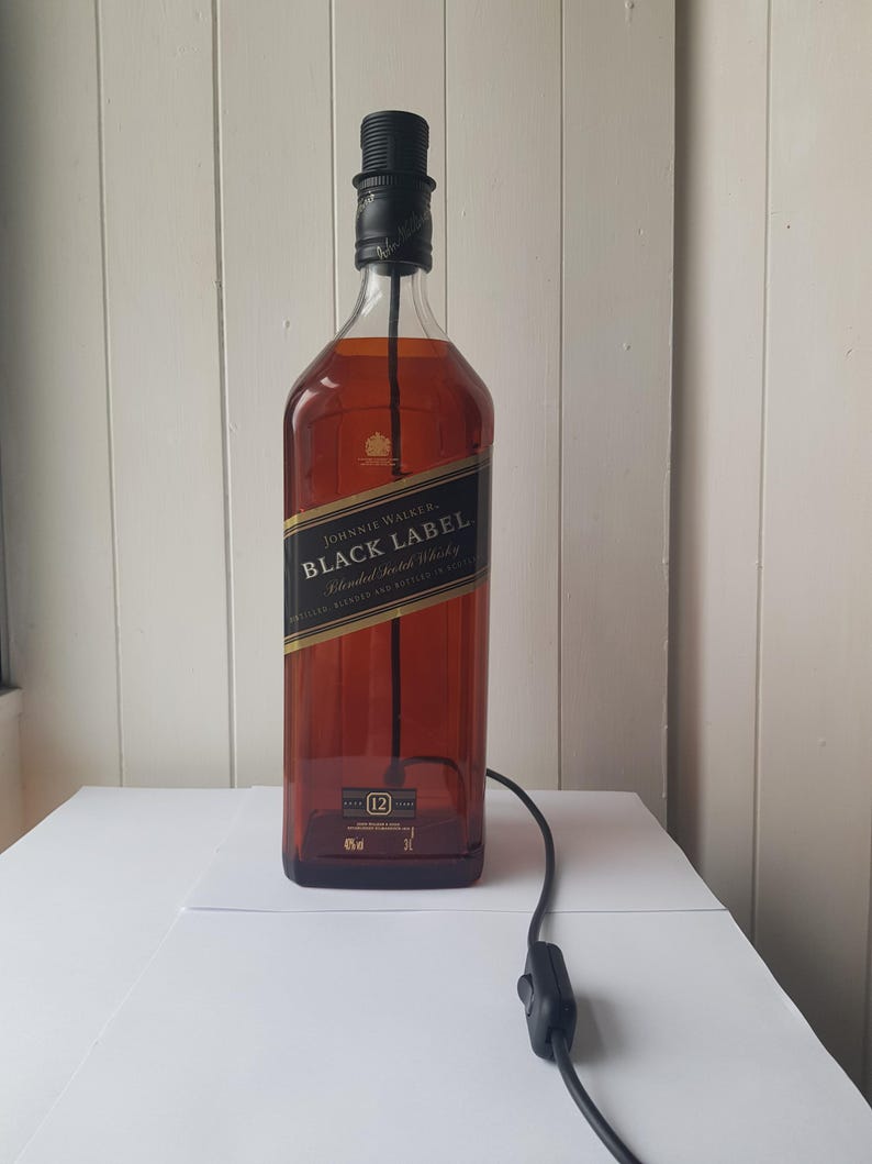 May include: A repurposed Johnnie Walker Black Label whiskey bottle transformed into a lamp. The amber-colored glass bottle features a black label with gold lettering. A black lamp socket and cord with an on/off switch are attached.