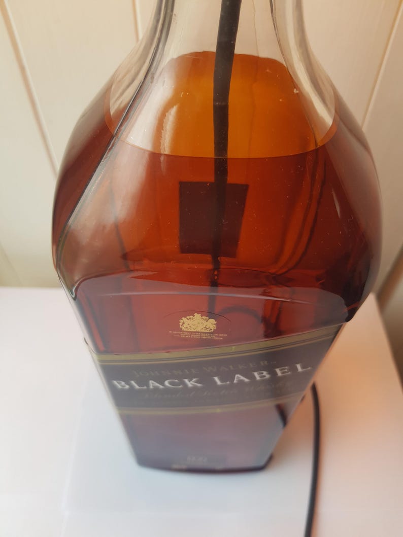 May include: A partially filled bottle of Johnnie Walker Black Label whiskey. The amber liquid is visible through the clear glass. The label is black and gold, with the brand name prominently displayed. A black cord extends from the bottle.
