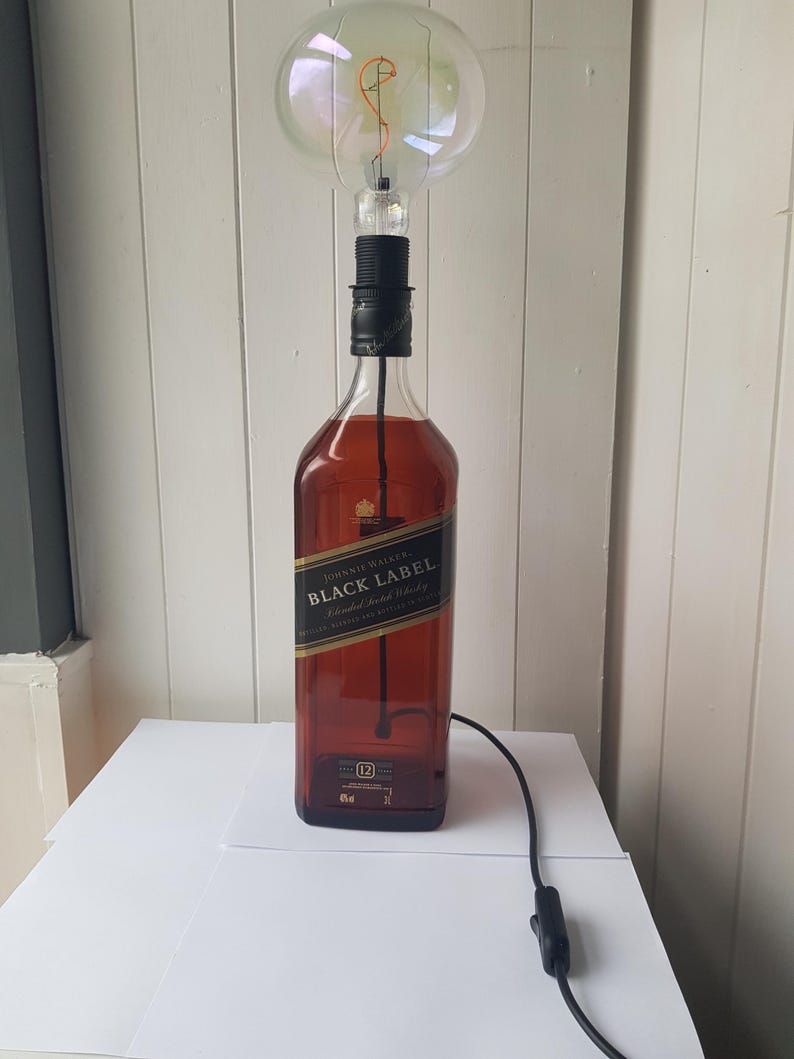 May include: A unique lamp made from a Johnnie Walker Black Label bottle. The lamp features a large, round light bulb and a black cord with an on/off switch. The bottle has a black and gold label.