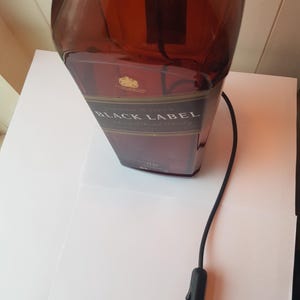 May include: A repurposed lamp made from a Johnnie Walker Black Label bottle. The brown glass bottle has a black label with gold lettering. A black cord with an on/off switch extends from the bottle.