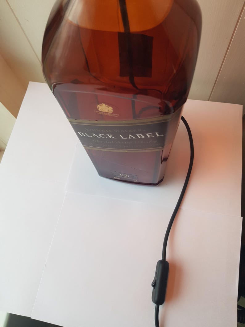 May include: A repurposed lamp made from a Johnnie Walker Black Label bottle. The brown glass bottle has a black label with gold lettering. A black cord with an on/off switch extends from the bottle.