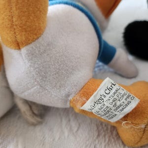 Puede incluir: Primer plano de un peluche de Donald Duck. El juguete tiene un cuerpo blanco, piernas naranjas y una camisa azul. Una etiqueta en la pierna dice "Mickey's Christmas". El juguete est&aacute; sobre una superficie blanca.
