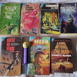 May include: A collection of vintage science fiction paperback books with colorful covers. Titles include "Kalin," "The Jester at Scar," "Technos," "The Temple of Truth," "Battle on Venus," "Recoil," and "Land Beyond the Map." A Pez dispenser is also present.