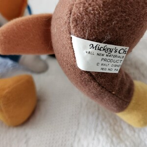 Puede incluir: Primer plano de un juguete de peluche marr&oacute;n con un ala marr&oacute;n y un pie amarillo. Una etiqueta blanca dice "Mickey's Ch... ALL NEW MATERIALS PRODUCT &copy; WALT DISNEY REG. NO. PA".