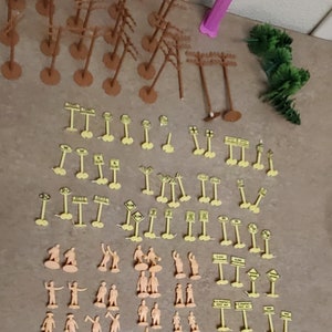 May include: A collection of miniature plastic figures, trees, and road signs for model railroading or other miniature scenes. The figures are beige, the trees are brown, and the signs are yellow with black lettering.