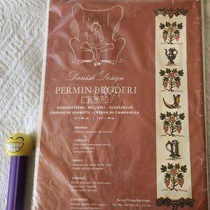 May include: A cross-stitch kit by Danish Design, featuring a design of grapes and other motifs. The kit is in a plastic sleeve and includes the text "PERMIN-BRODERI". The kit measures 6 1/2 inches by 39 inches.