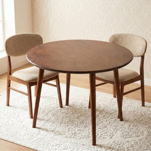 Puede incluir: Una mesa de comedor redonda de madera marrón oscuro con cuatro patas cónicas, acompañada de dos sillas con estructuras de madera marrón oscuro y tapicería de tela texturizada de color beige claro en los respaldos y asientos curvos.