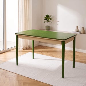 Op de afbeelding: Een rechthoekige tafel met een glad, levendig groen tafelblad met afgeronde hoeken. De tafel wordt ondersteund door vier taps toelopende, cilindrische poten in een bijpassende donkergroene kleur, met een lichtbeige frame.
