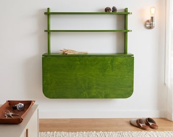 May include: A wall-mounted, fold-down desk in a vibrant green wood finish, featuring two open shelves above the main surface. The desk is shown in its closed, vertical position, displaying a smooth, rectangular wooden panel with rounded corners.