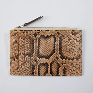 May include: A rectangular wallet with a snakeskin pattern in shades of brown and black. The wallet has a zipper closure at the top and several card slots. The zipper pull is brown.
