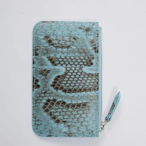 Puede incluir: Tarjetero azul claro con estampado de piel de serpiente. La cartera tiene m&uacute;ltiples ranuras para tarjetas y un compartimento con cremallera. El tirador de la cremallera tambi&eacute;n es azul claro. El tarjetero est&aacute; hecho de un material texturizado.