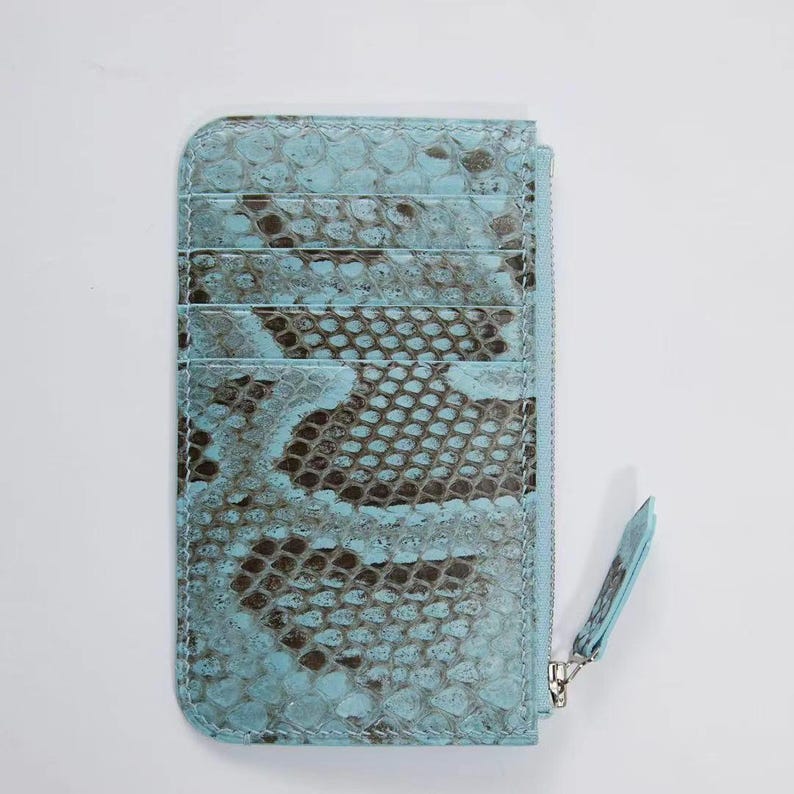 Puede incluir: Tarjetero azul claro con estampado de piel de serpiente. La cartera tiene m&uacute;ltiples ranuras para tarjetas y un compartimento con cremallera. El tirador de la cremallera tambi&eacute;n es azul claro. El tarjetero est&aacute; hecho de un material texturizado.