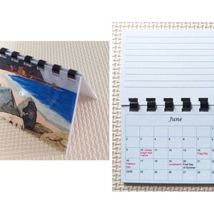 May include: A small desk calendar with a spiral binding. The calendar shows the month of June with a beach scene on the cover. The calendar is open, displaying the days of the month and lined paper.