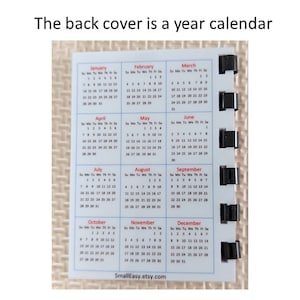 May include: A small, rectangular year calendar with a white background. The calendar displays all twelve months, with each month's days arranged in a grid. The text "The back cover is a year calendar" is at the top. The Etsy shop name is at the bottom.