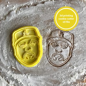 May include: A yellow 3D-printed cookie cutter in the shape of a man's face wearing a baseball cap with the letter "A". Next to it is a cookie cut-out. The image includes the text "3D printing cookie cutter STL file".