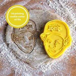 Puede incluir: Un cortador de galletas amarillo con la forma de una persona con una gorra de béisbol, junto a una galleta con la misma cara presionada. El cortador de galletas tiene las palabras "Los Angeles Army" en la gorra. La imagen también incluye el texto "3D printing cookie cutter stl file".