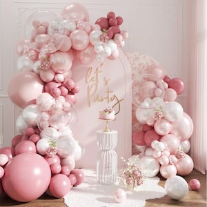 May include: A party scene with a pink and white balloon arch, a small cake, and the words "Let's Party" in gold script. The balloons are in various shades of pink and white, with some clear bubble balloons.