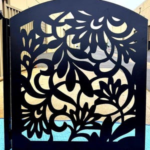 May include: Black metal garden gate with a floral design. The gate features an arched top and intricate cut-out patterns of leaves and flowers, creating a decorative and open appearance. The gate is designed for outdoor use.