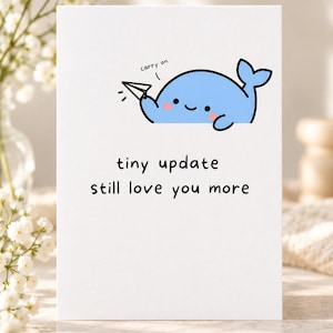 May include: A white greeting card featuring a cartoon light blue whale holding a paper airplane with the text "carry on" above it. Below the whale, the text reads "tiny update still love you more" in a simple black sans-serif font.